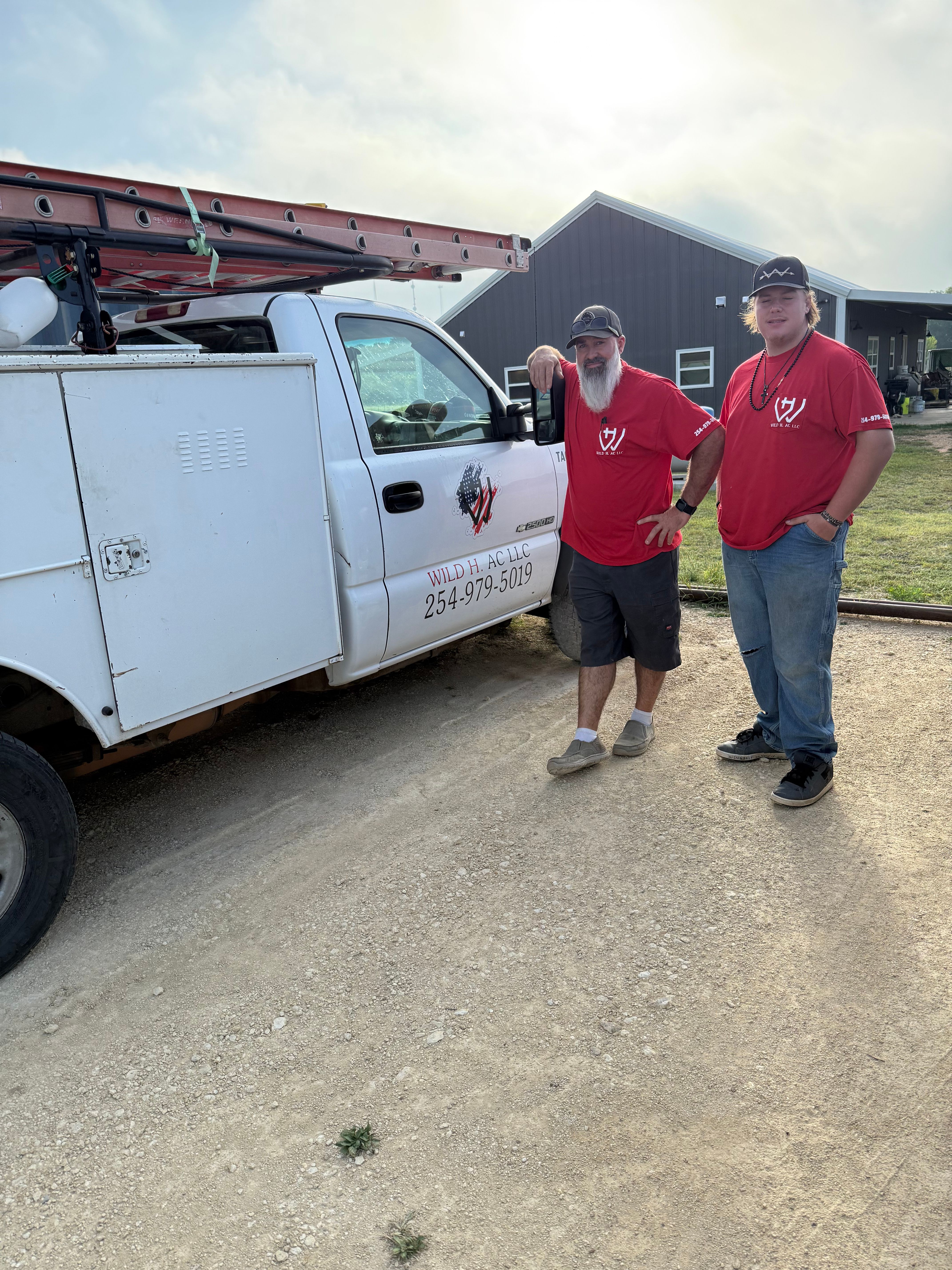 Wild H AC LLC Team — Owner & Service Tech, Dublin TX Wild H AC LLC service technician and owner in red company shirts standing beside the service truck in Dublin, TX